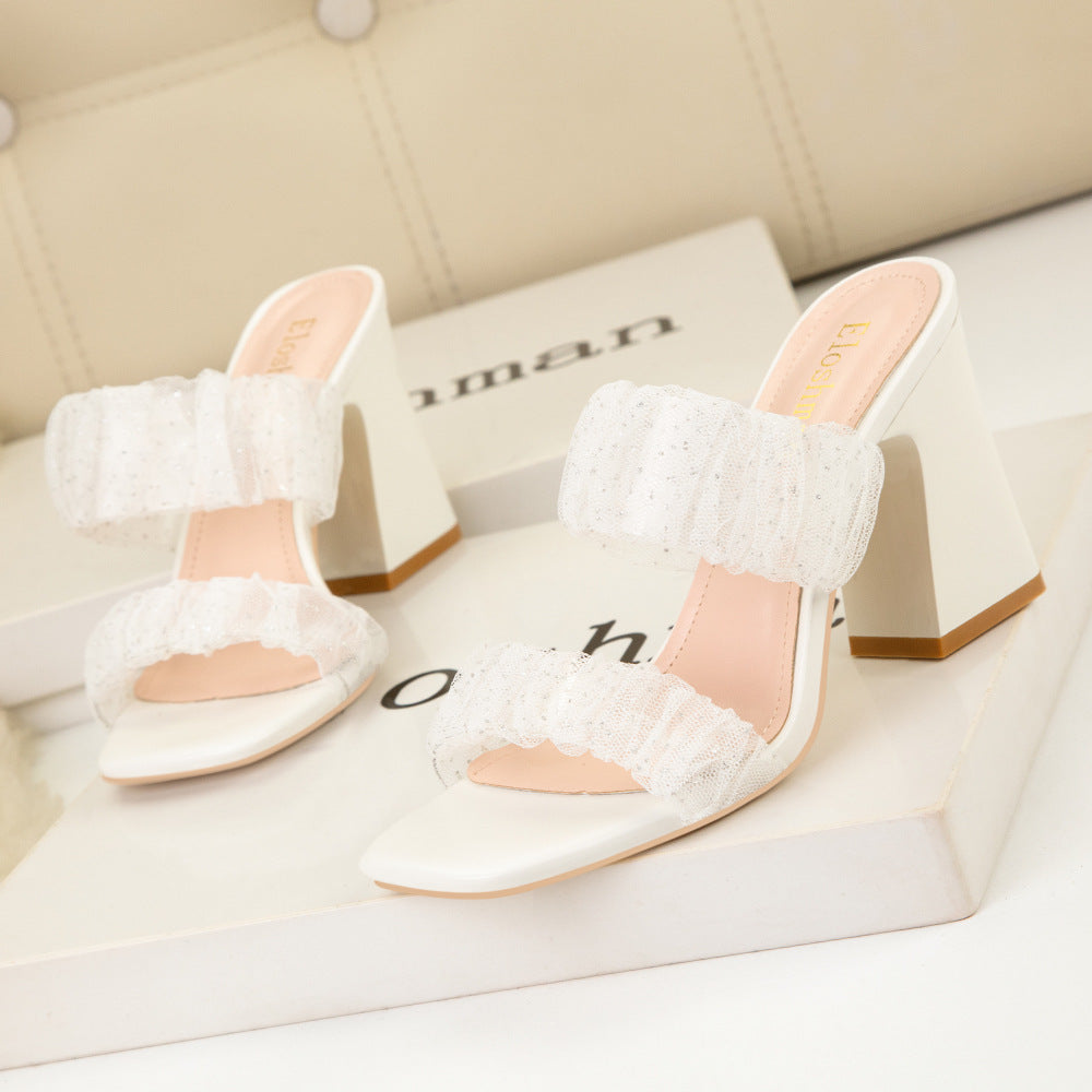 A pair of open toed square lace sandals with sparkling straps, placed on a flat surface. white